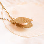 Angled view of gold scallop shell necklace with freshwater pearl pendant