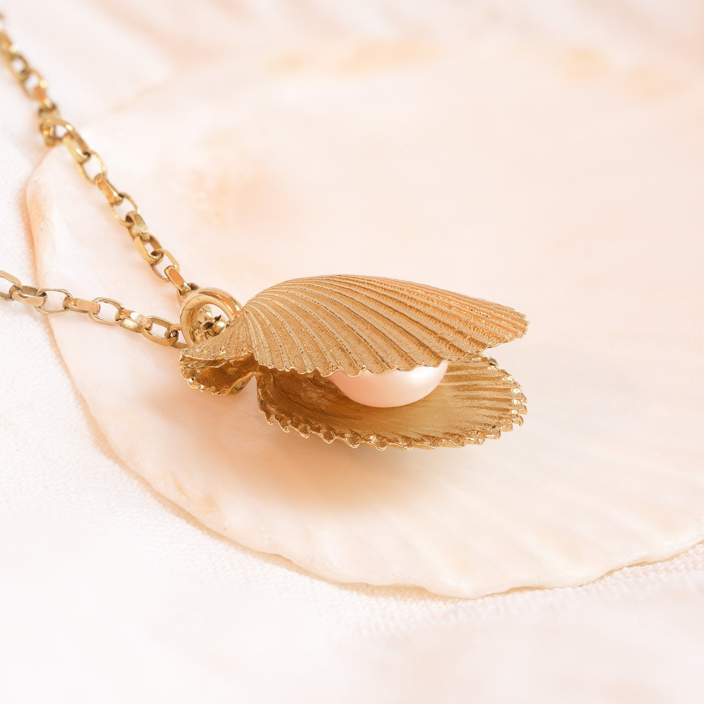 Angled view of gold scallop shell necklace with freshwater pearl pendant
