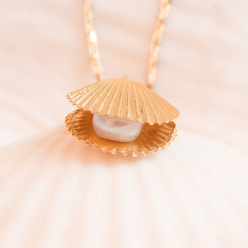 Gold scallop shell necklace with freshwater pearl on light background close-up