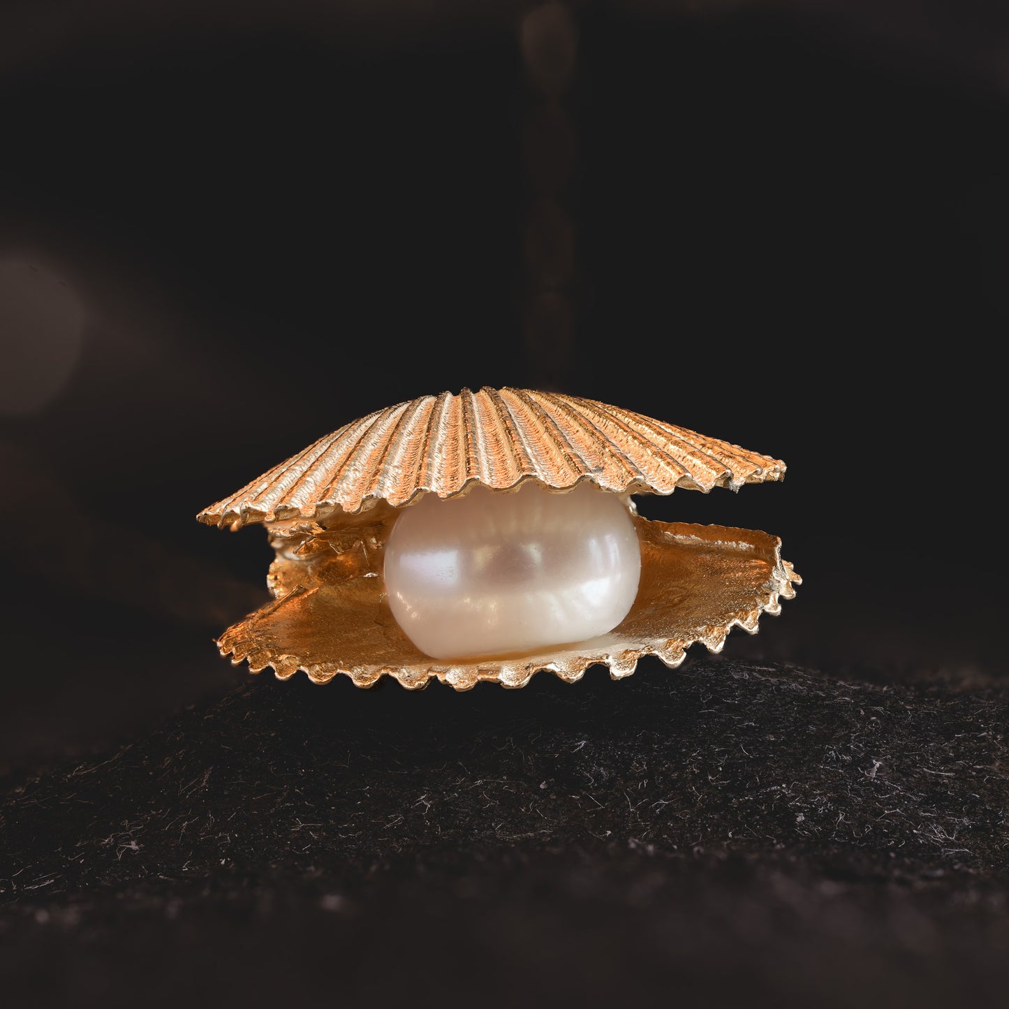 Gold double scallop shell necklace with freshwater pearl close-up on dark background